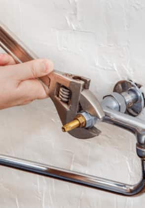 Person repairing faucet pipe with a tool.