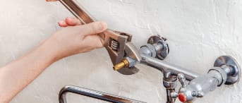 Une personne réparant un tuyau de robinet avec un outil.