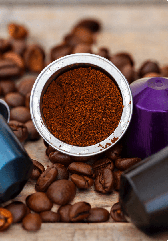 An open coffee pod surrounded by coffee pods and roasted coffee beans.