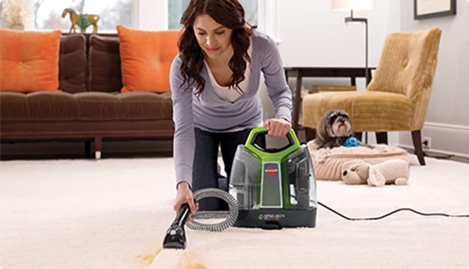 Woman using a Bissell Little Green ProHeat® Pet Portable Carpet & Upholstery Cleaner.