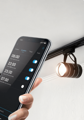 Une main tenant un téléphone intelligent avec une appli d’éclairage intelligent sur l’écran devant une rangée de plafonniers. 