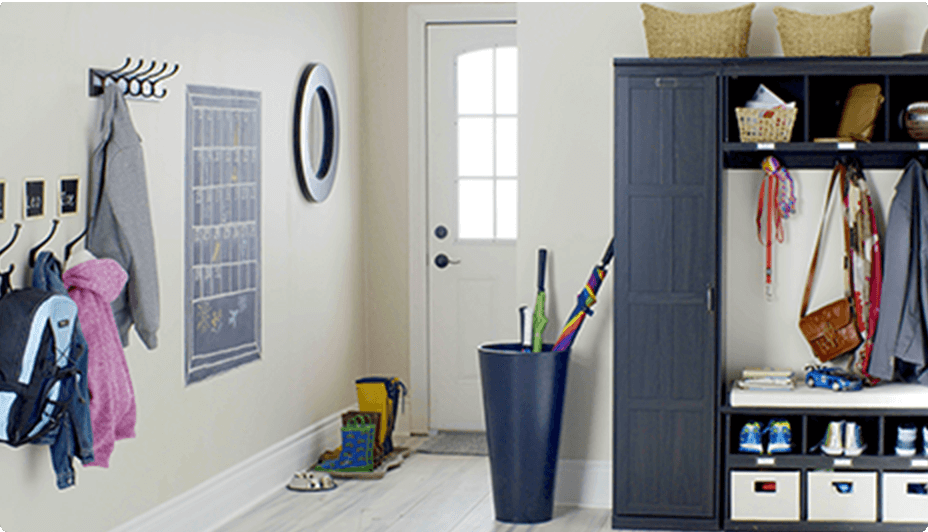 A home entryway with wall mirror, wall hooks with coats, umbrellas in a large bin, and  a coat and shoe storage unit in black.
