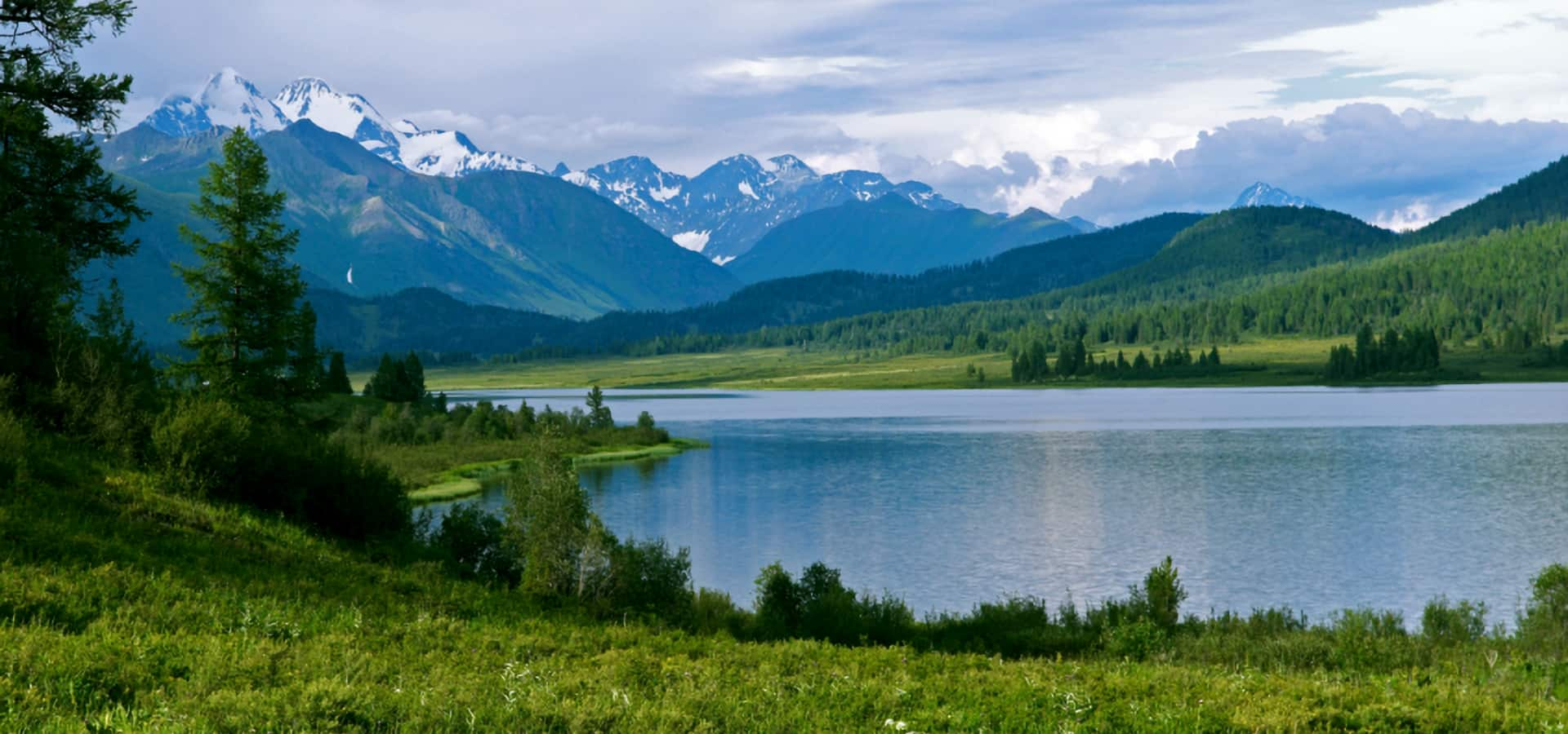 Open landscape with a lake, hills, trees and mountains in the background.