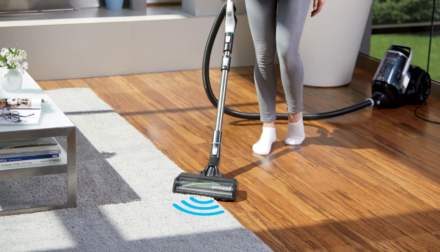 Woman uses a canister vacuum on a white rug.