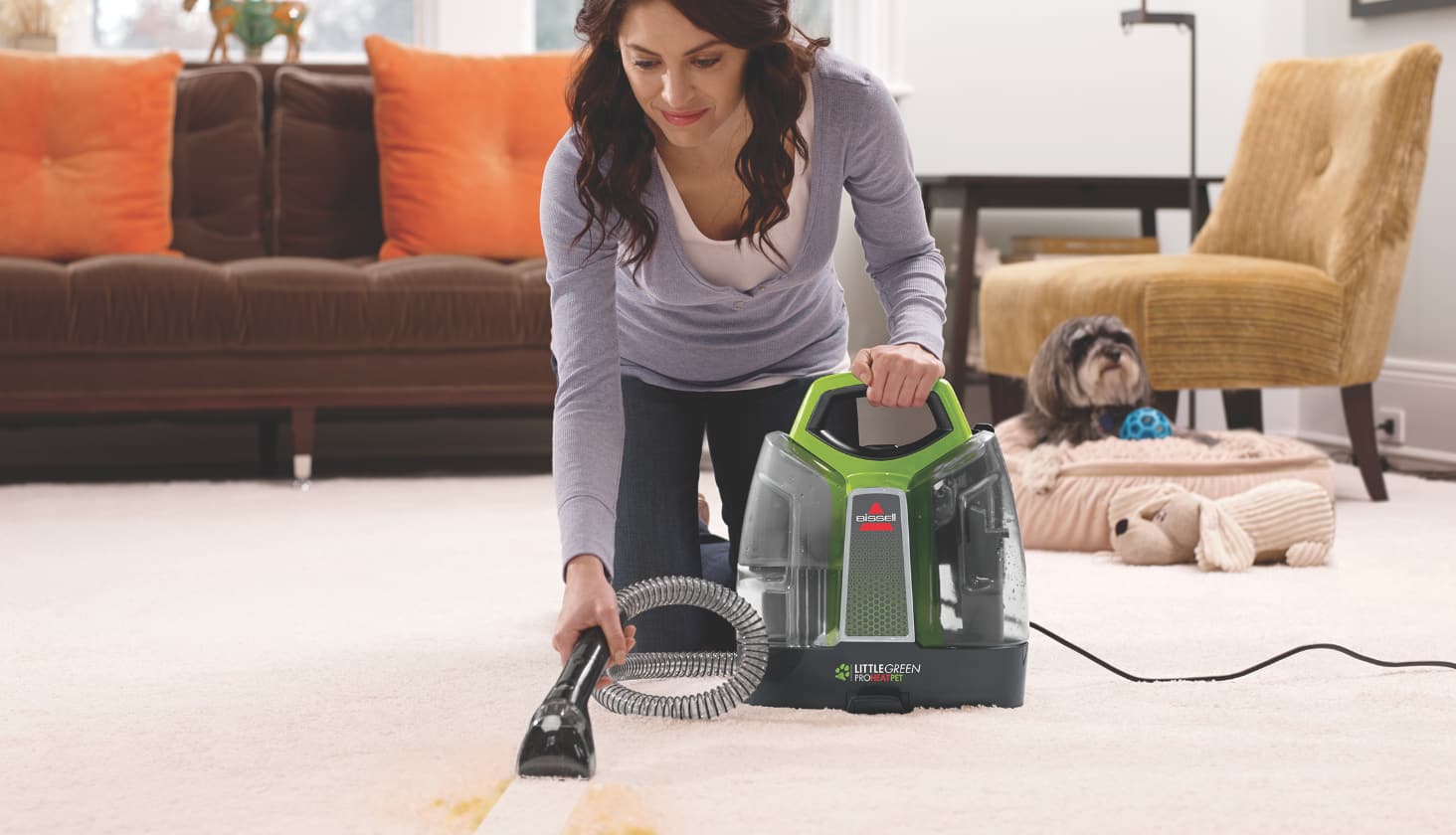 Woman uses a Bissell Little Green ProHeat® Pet Portable Carpet & Upholstery Cleaner to removal a yellow stain on a white living room carpet. 