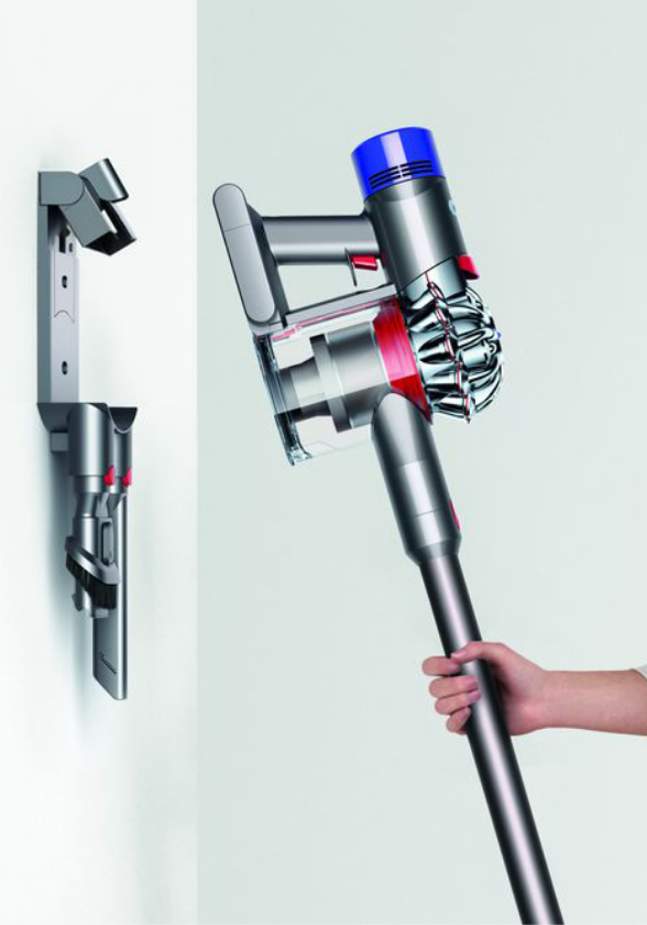 Woman about to place a stick vacuum on a wall-mounted storage rack,