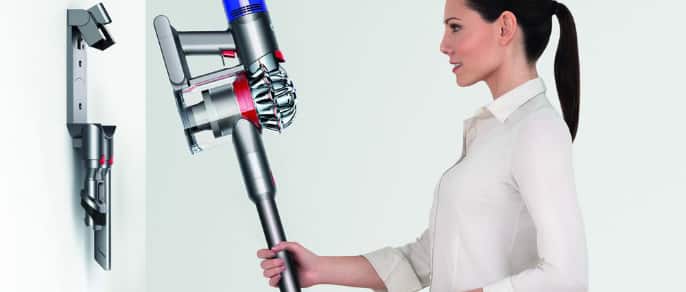 Woman about to place a stick vacuum on a wall-mounted storage rack,