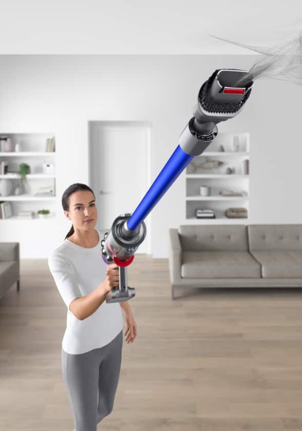 Woman uses a stick vacuum in handheld mode to clean an area above her head.