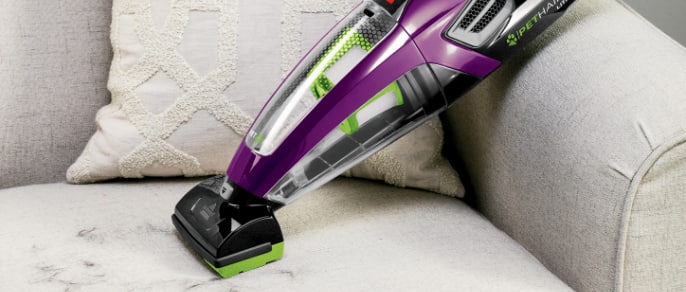 Person uses a handheld vacuum on a white sofa.