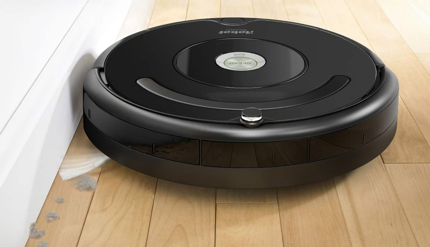 iRobot Roomba vacuum on a hardwood floor next to a wall.