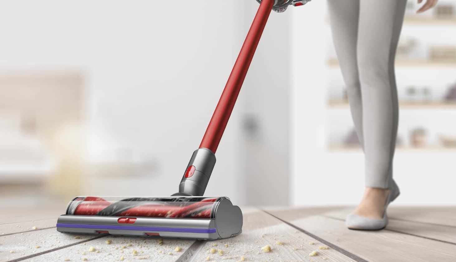  Woman uses a stick vacuum to clean up crumbs on a living room rug.