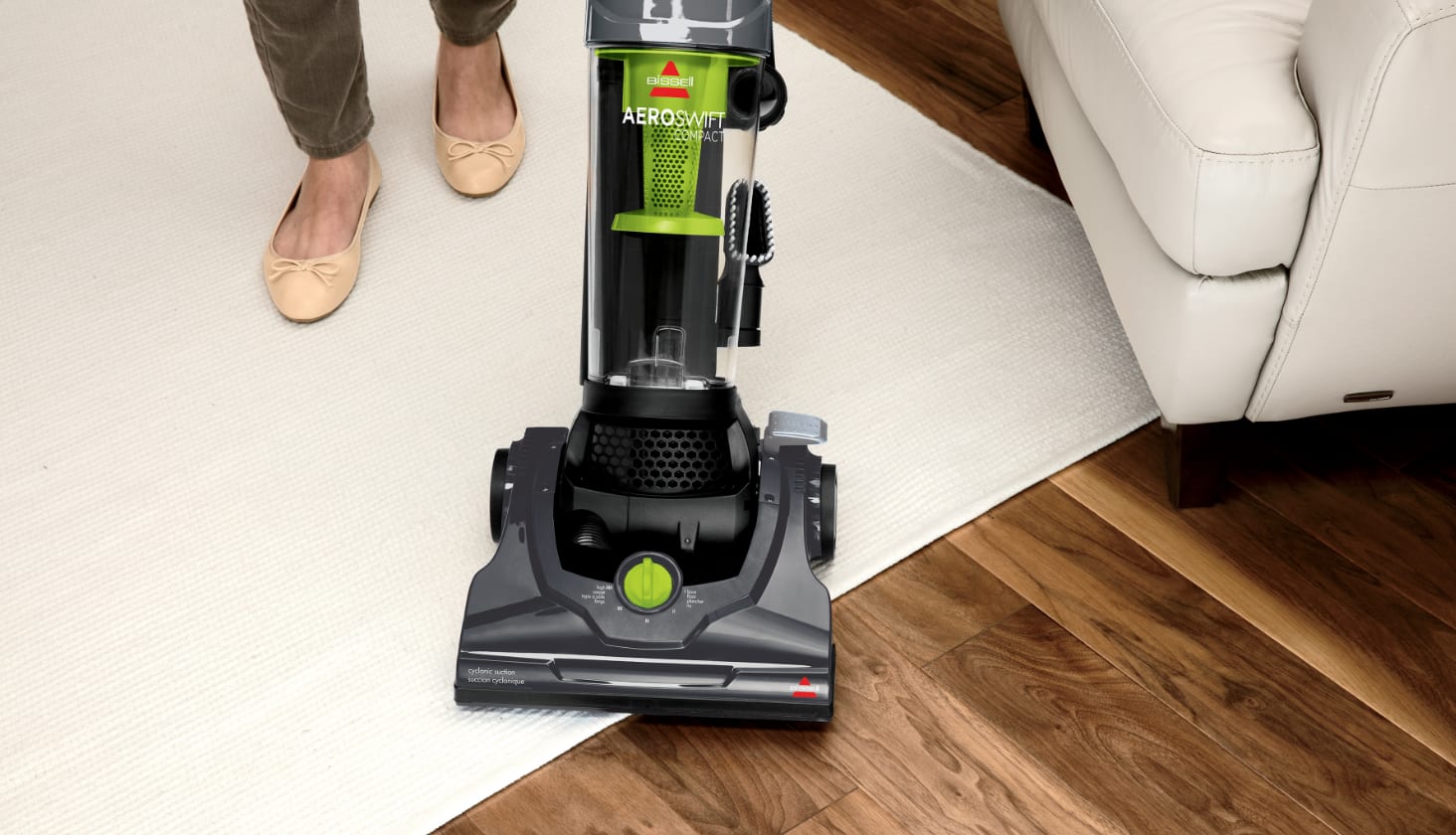 Woman uses an upright Bissell vacuum on a white living room rug.
