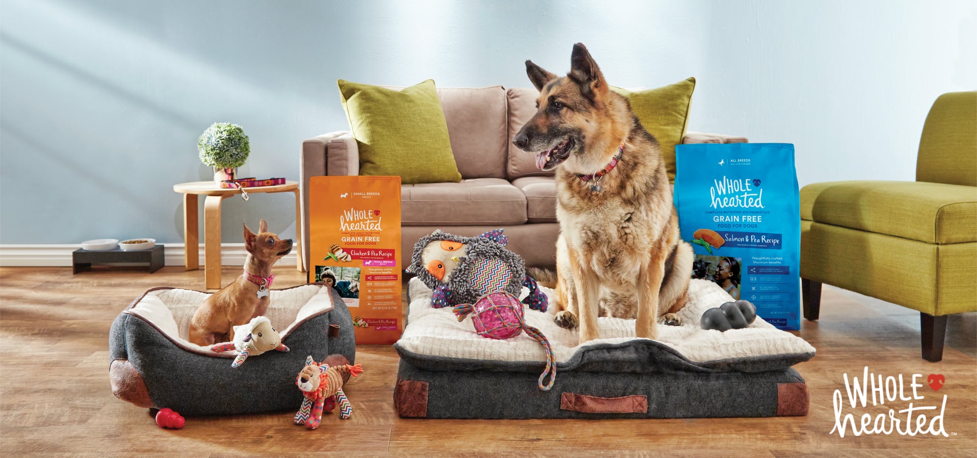 Two large Wholeheated dry dog food bags behind two dogs sitiing on dog beds in a living room setting. 