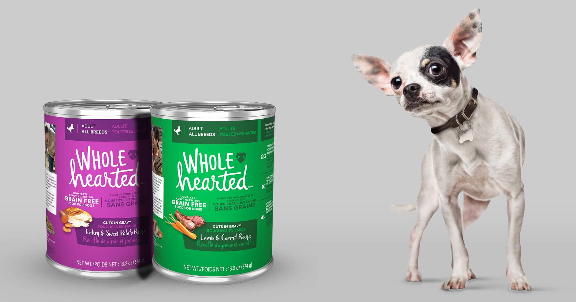 Small black and white dog standing next to two cans of Wholehearted wet dog food.