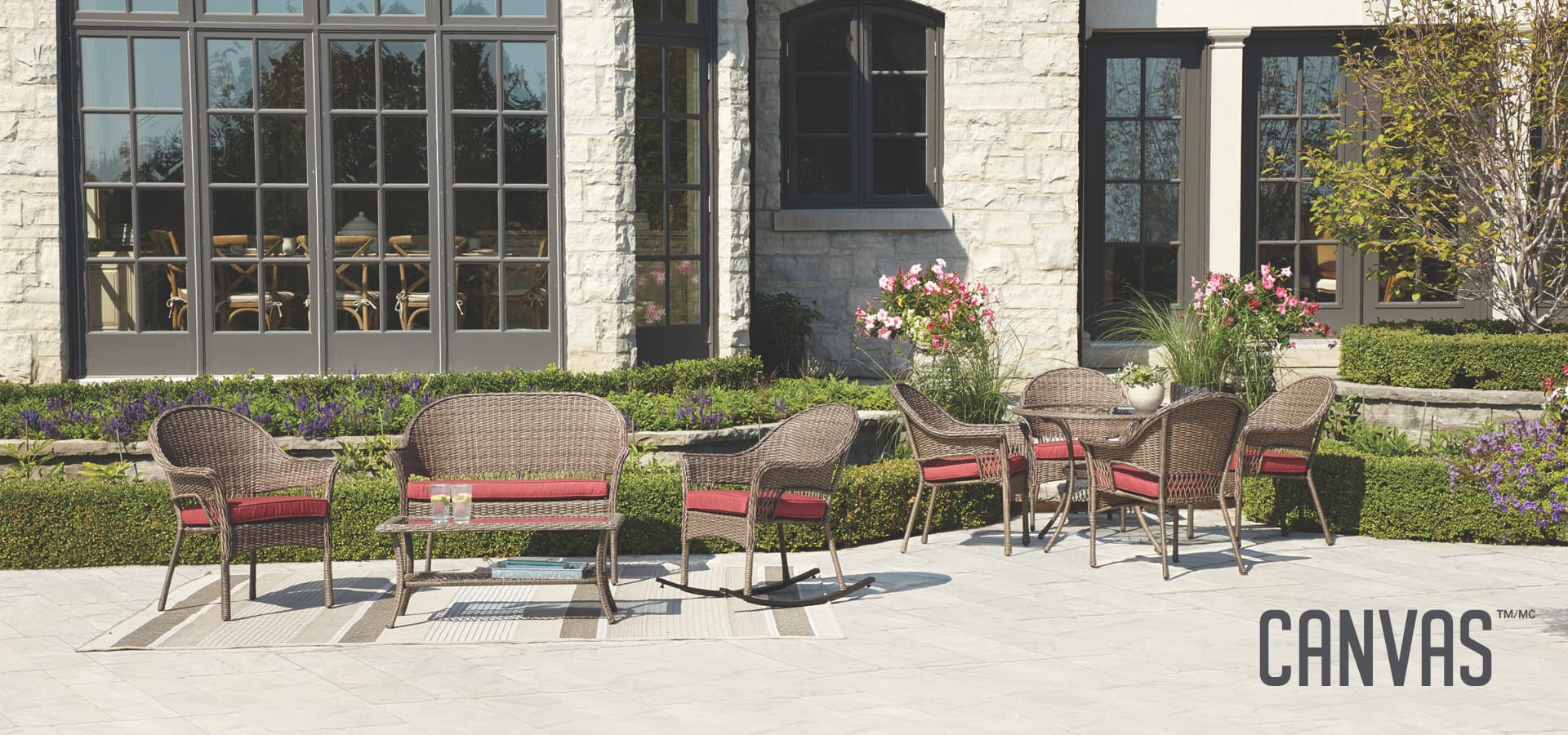 Outdoor area with an outdoor loveseat and two accompanying outdoor chairs, as well as a patio table set surrounded by four wicker patio chairs. 