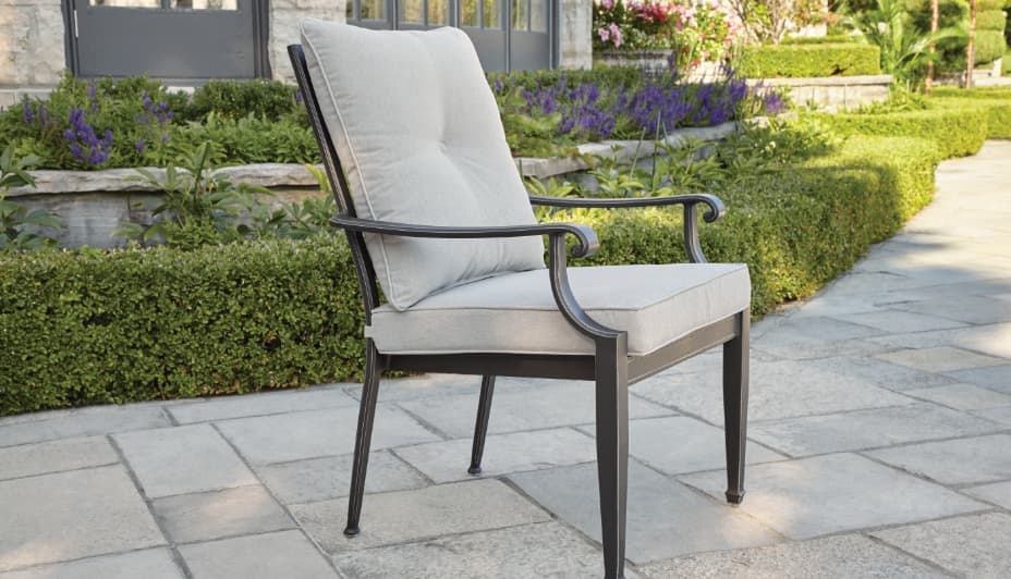 A single, simple, metal outdoor dining armchair with grey cushions on the back and the seat. 