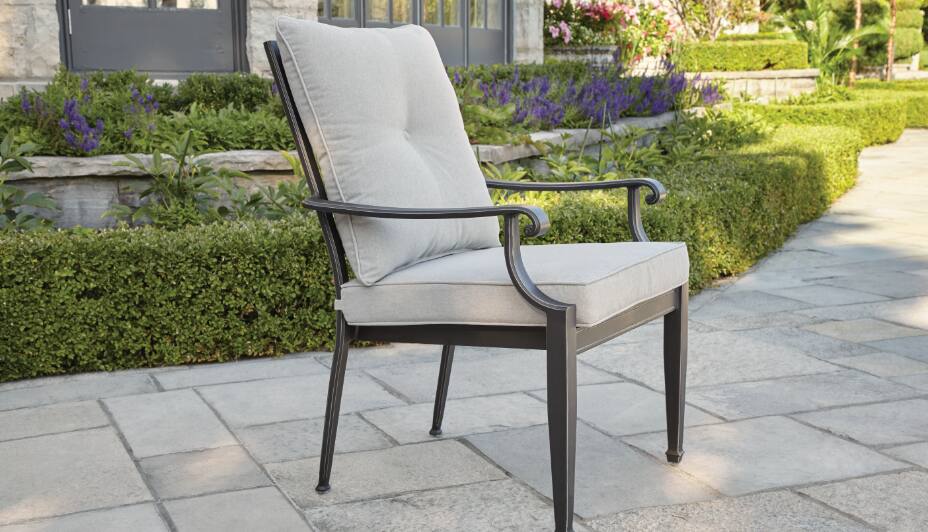 Une grande table à dîner ronde entourée de quatre chaises à coussin dans un jardin Chaise à dîner de jardin CANVAS Coventry Hills, gris tourterelle Construction robuste et durable  Un seul fauteuil de salle à dîner d'extérieur, simple, en métal, avec des coussins gris sur le dossier et le siège. 