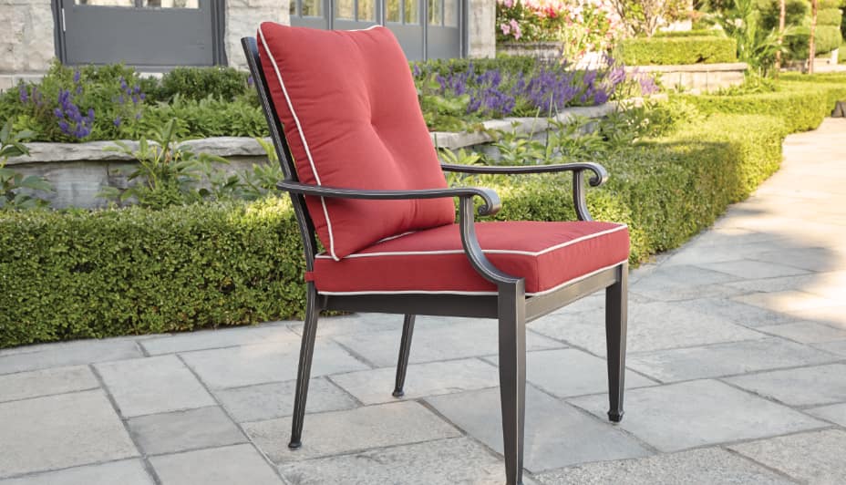 Un seul fauteuil de salle à dîner d'extérieur, simple, en métal, avec des coussins rouges sur le dossier et le siège.