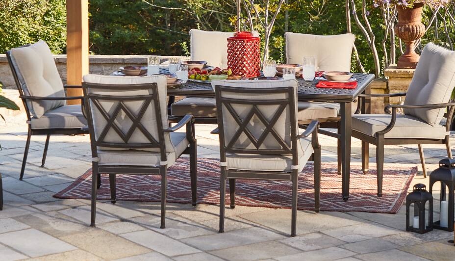 A large, rectangular outdoor dining table surrounded by six cushioned chairs in a designated backyard dining area. 