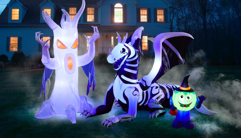 Fantôme gonflable, squelette de dragon et goule illuminée sur une pelouse avec du brouillard devant une maison.