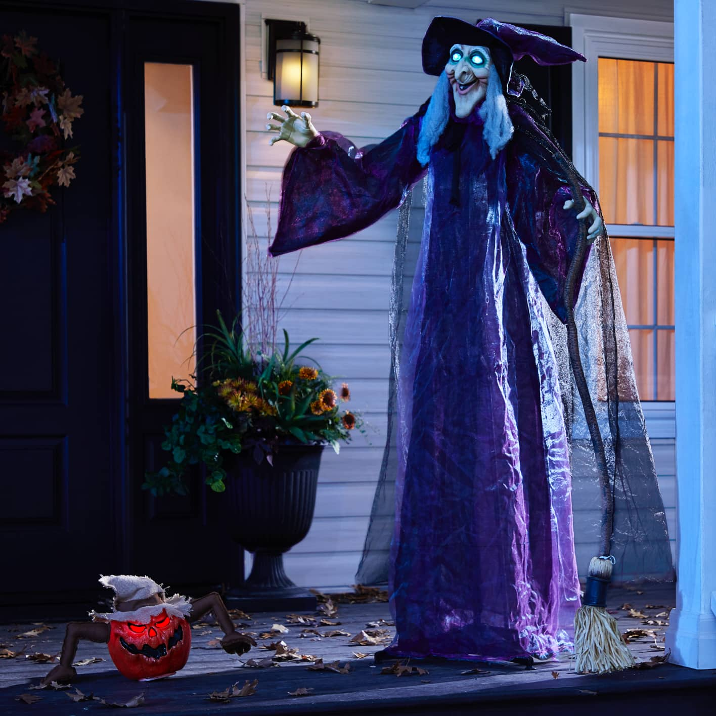 Full-sized animated witch figure standing on a front porch at night.