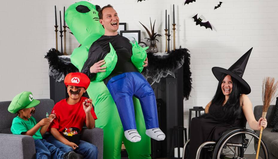 Man wearing an alien costumes with a woman dressed as a witch and two boys wearing Luigi and Mario costumes at home.
