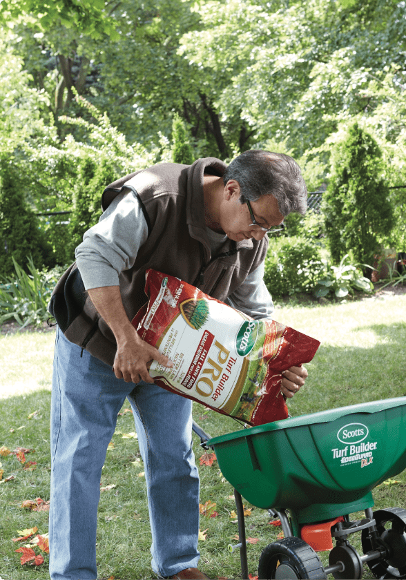 A man pouring weed prevent fertilizer in a Scotts Turf Builder Mini Edgeguard. 