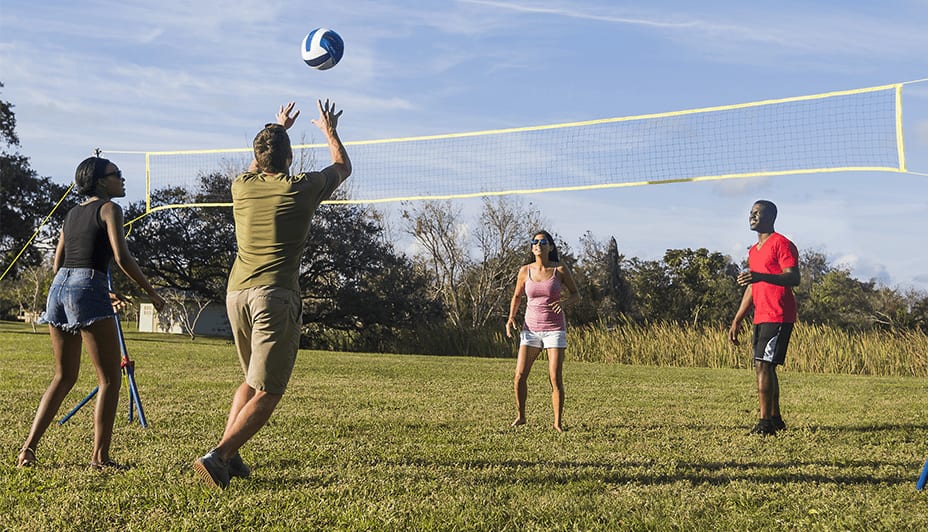 Group of 2 men and 2 women play volleyball outdoors.