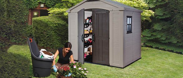 Standard-sized grey garden shed placed on grass with woman kneeled in front of it while gardening. 