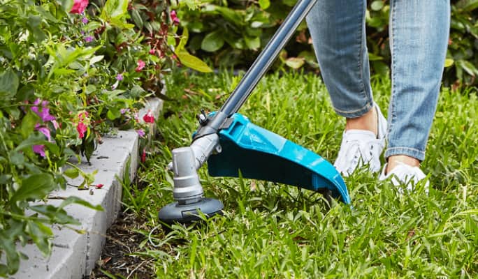Person with jeans and white shoes using grass trimmer