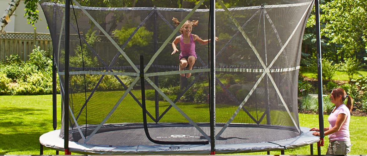 Young, happy girl jumping in the middle of a safely enclosed backyard trampoline.