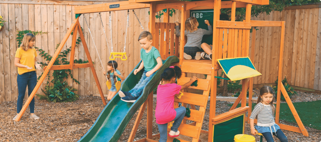 Des enfants se balançant, glissant et jouant joyeusement dans un centre de jeux en bois dans le jardin.