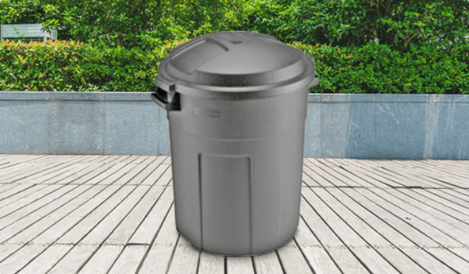 A dark-grey 77-litre Rubbermaid Refuse Can stands on a wooden deck in front of a stand of trees.