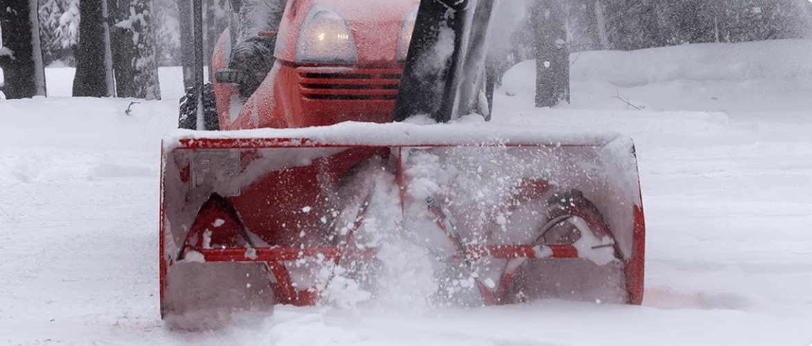 A closeup image of the blade housing of a red snowblower clearing snow from a residential driveway. 