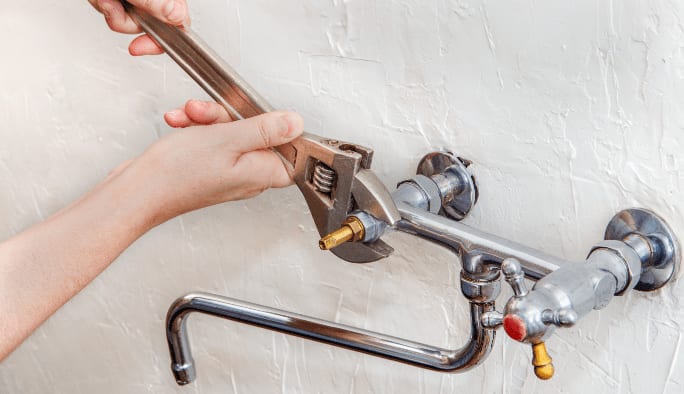 Gros plan de mains utilisant une clé sur les tuyaux d’un lavabo