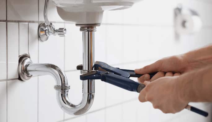 Close-up of hands using a wrench on a sink’s pipes.