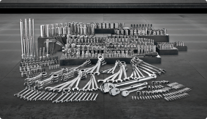 A wide array of hand tools, including wrenches, sockets, and bits, set against a grey background.