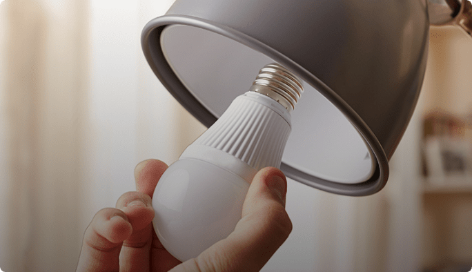A hand inserts a lightbulb into a grey lamp.