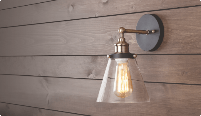 A grey-and-gold light fixture with an illuminated bulb mounted to a brown wood-panelled wall.