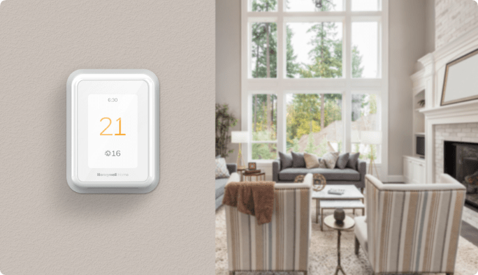 Un thermostat intelligent blanc affichant « 21 °C » monté sur un mur beige près d’un salon ensoleillé.