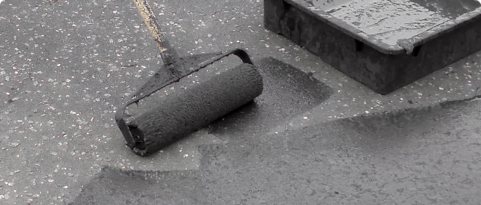 A roller brush blackened with driveway sealer applies the substance to an asphalt driveway.