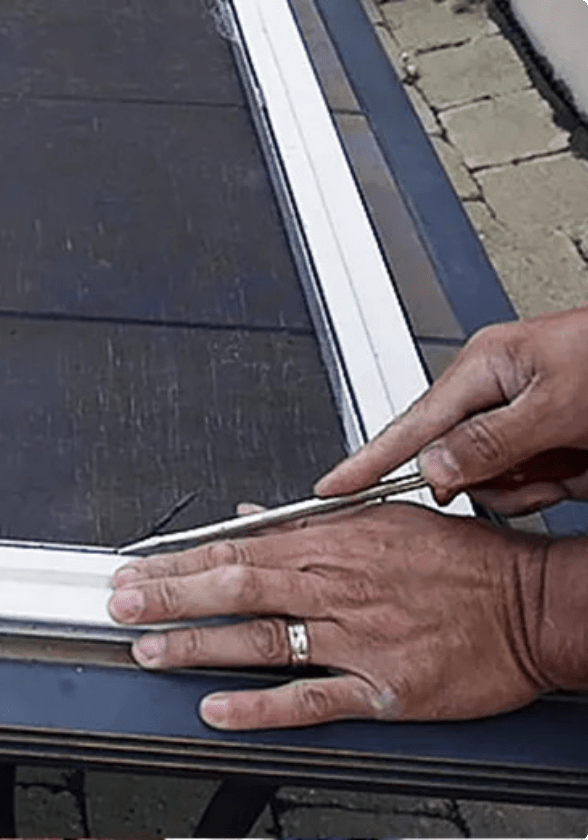 Hands use the blade of a screwdriver to insert wire mesh into the frame of a white screen door.