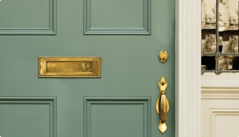 Une porte d’entrée verte fermée avec un trou de serrure, une poignée de porte et une fente à lettre dorés.