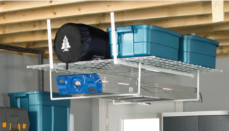 A rolled-up sleeping bag and two blue storage bins rest on a white storage rack suspended from the ceiling of a garage.