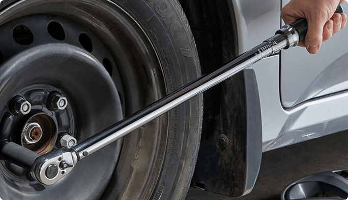 Une main utilisant une clé à écrous argentée sur un écrou d’un pneu d’auto.