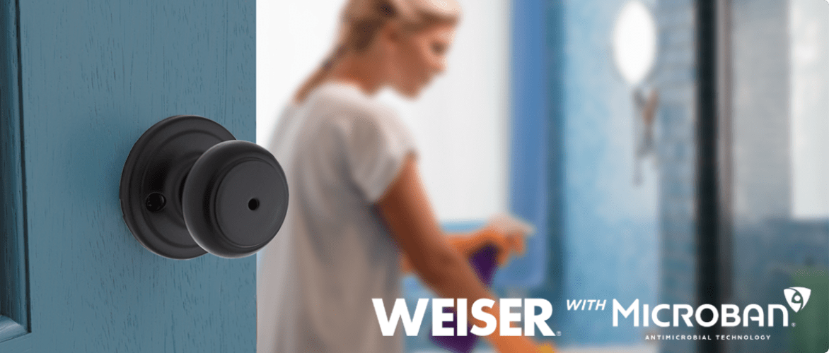 Black round Weiser Microban doorknob handle on bathroom door. Woman cleaning in background.