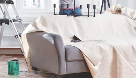 Une bâche couvrant un canapé avec une boîte de peinture se trouvant à côté de lui sur le sol.
