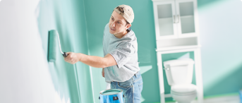 Man painting his bathroom’s wall with a roller.