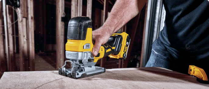 Man cutting wood with a black and yellow DeWalt jigsaw.