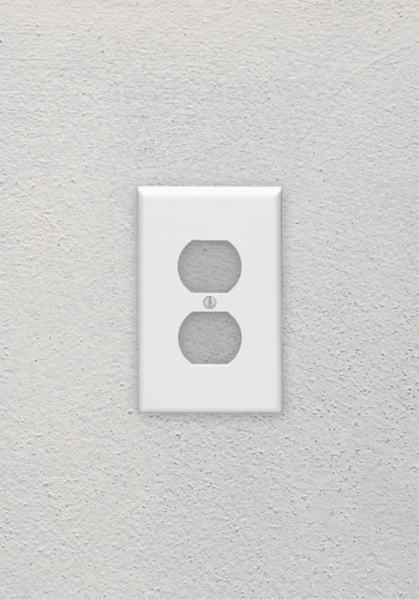 A white Leviton Duplex Device Receptacle Wallplate on a grey wall inside a home.